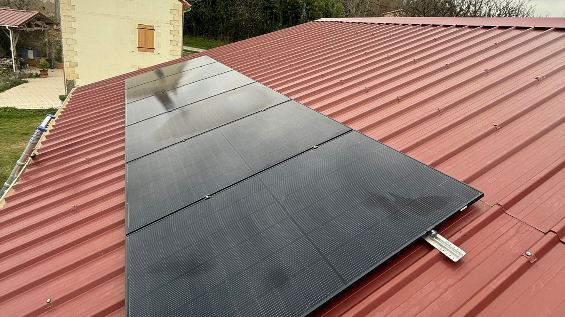 Panneaux solaires noirs montés sur un toit en tôle ondulée rouge, vus d'un angle élevé.