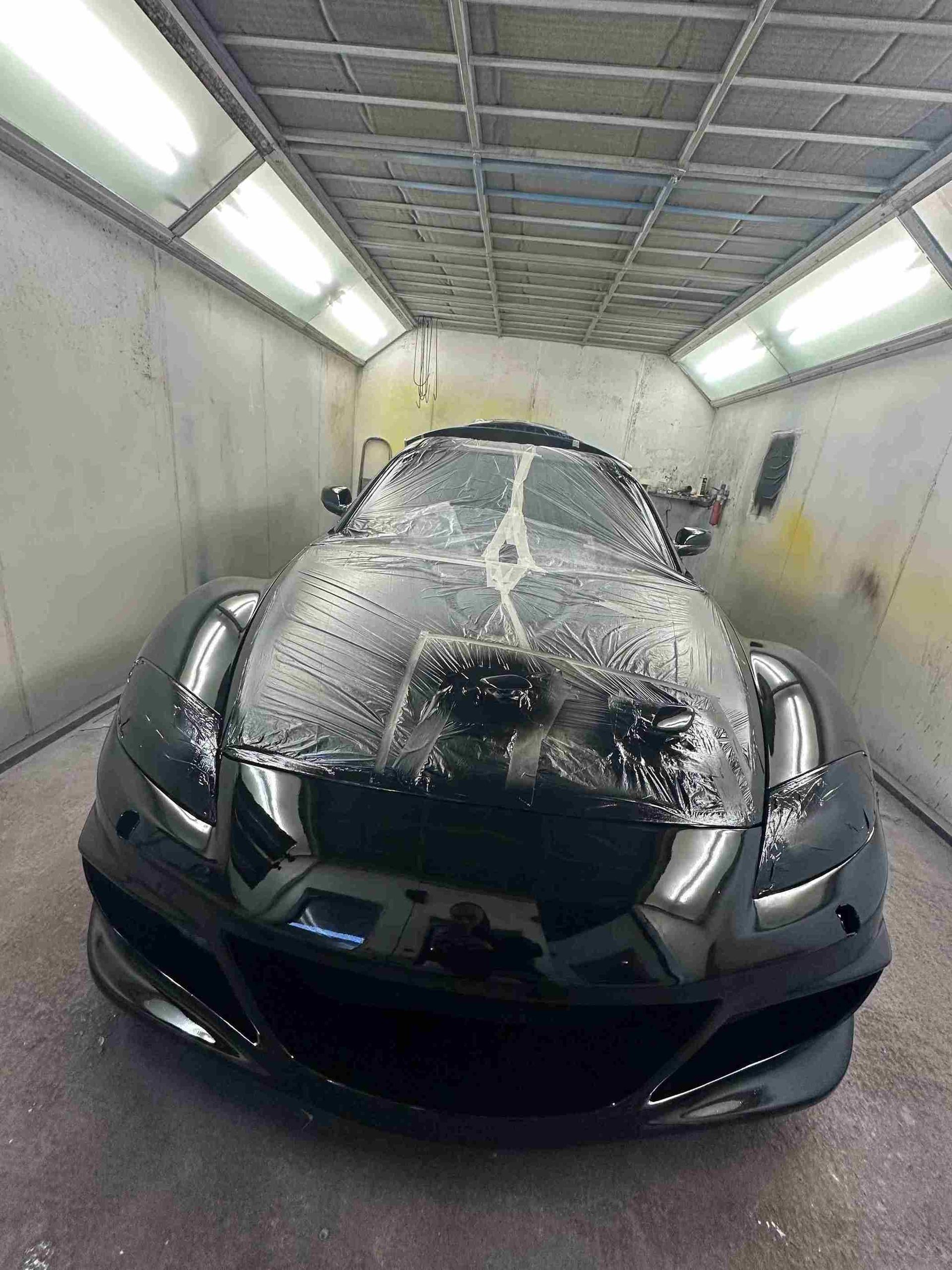 Un coche deportivo negro está en una cabina de pintura.