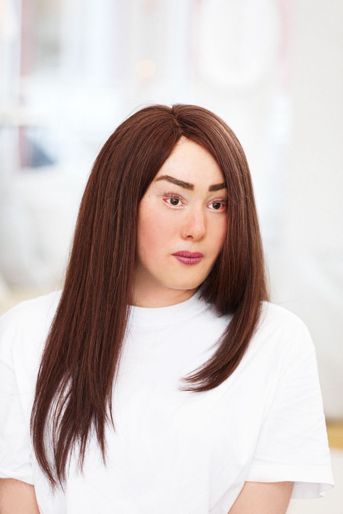 Eine Person mit langem braunem Haar und blasser Haut, die ein weißes T-Shirt trägt und nach unten schaut.