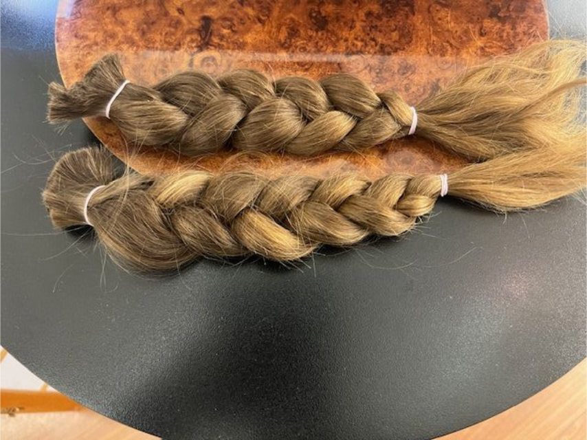 Zwei hellbraune, geflochtene Haarsträhnen mit Gummibändern.