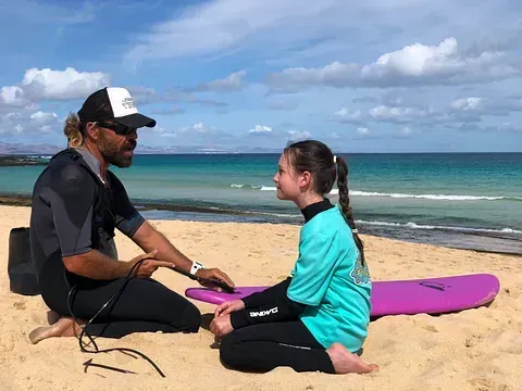 Un hombre y una niña están sentados en una playa con tablas de surf.