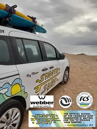 Una furgoneta con tablas de surf encima está aparcada en la playa.