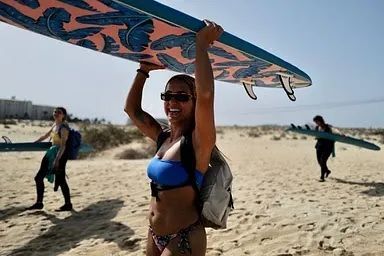 Una mujer en bikini lleva una tabla de surf sobre su cabeza.