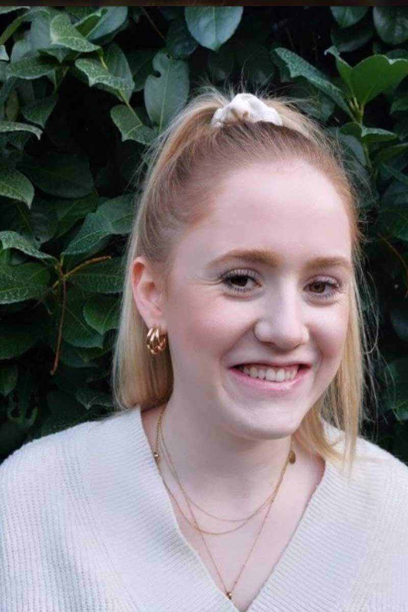 Junge Frau mit zurückgekämmten blonden Haaren, lächelnd. Grüner Hintergrund.