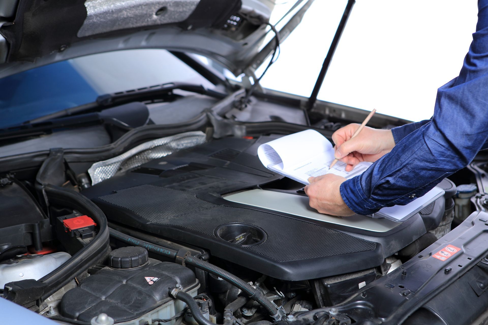 Moteur de voiture en contrôle technique examiné par un garagiste prenant des notes sur un bloc blanc