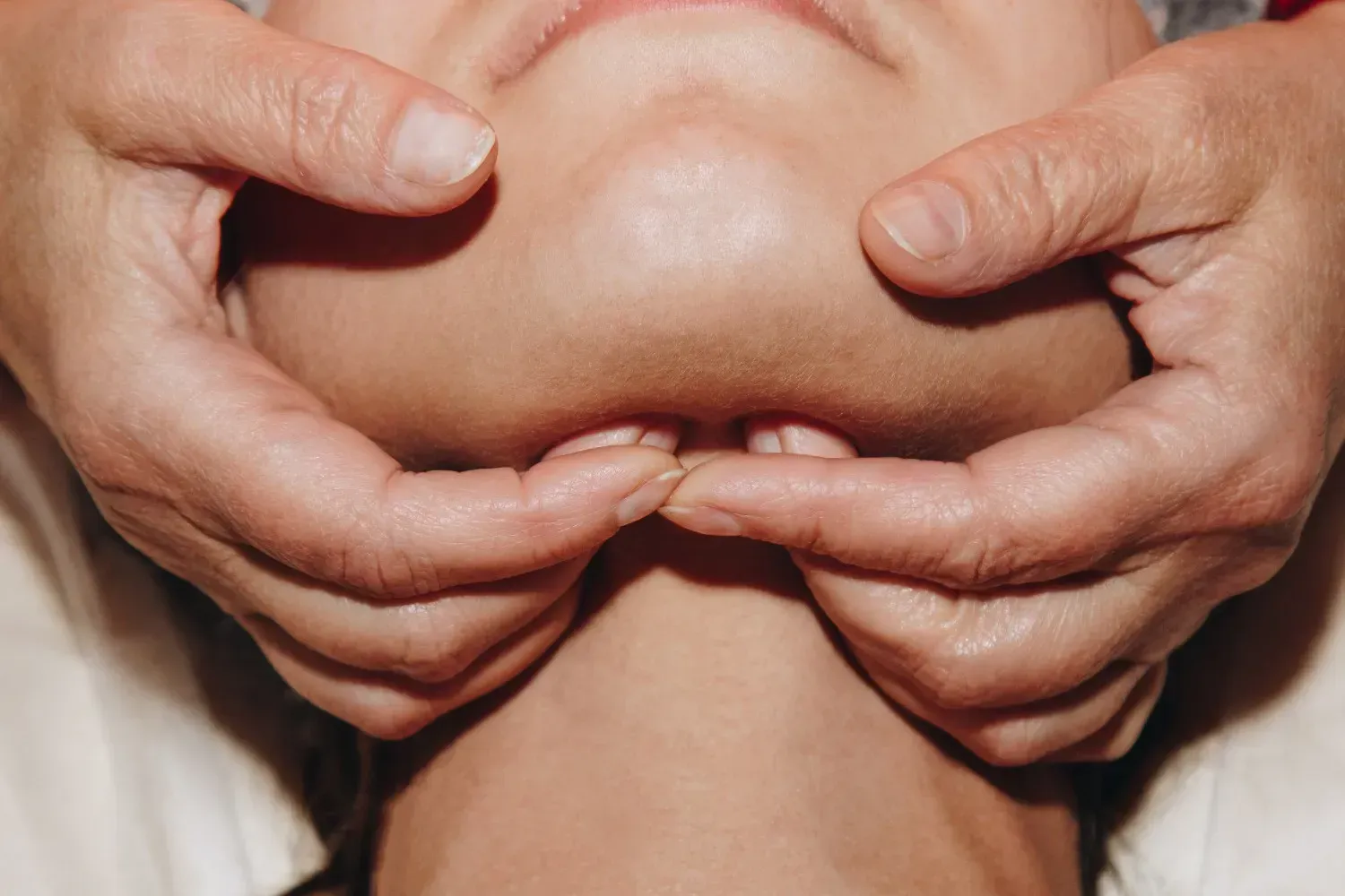 Manos masajeando la barbilla de una persona, posiblemente con fines terapéuticos.