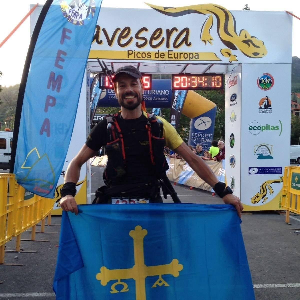 Hombre con bandera asturiana en la línea de meta de una carrera en los Picos de Europa, España.