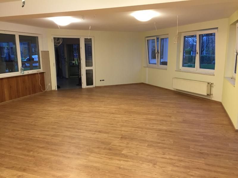 Ein großer leerer Raum mit Holzboden und Fenstern.