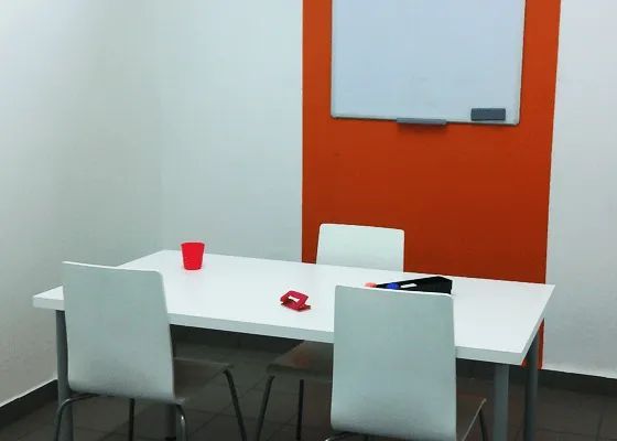 Uma sala com uma mesa e cadeiras e um quadro branco na parede