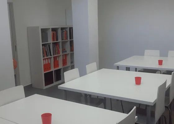 Uma sala com mesas e cadeiras brancas e xícaras vermelhas sobre elas.