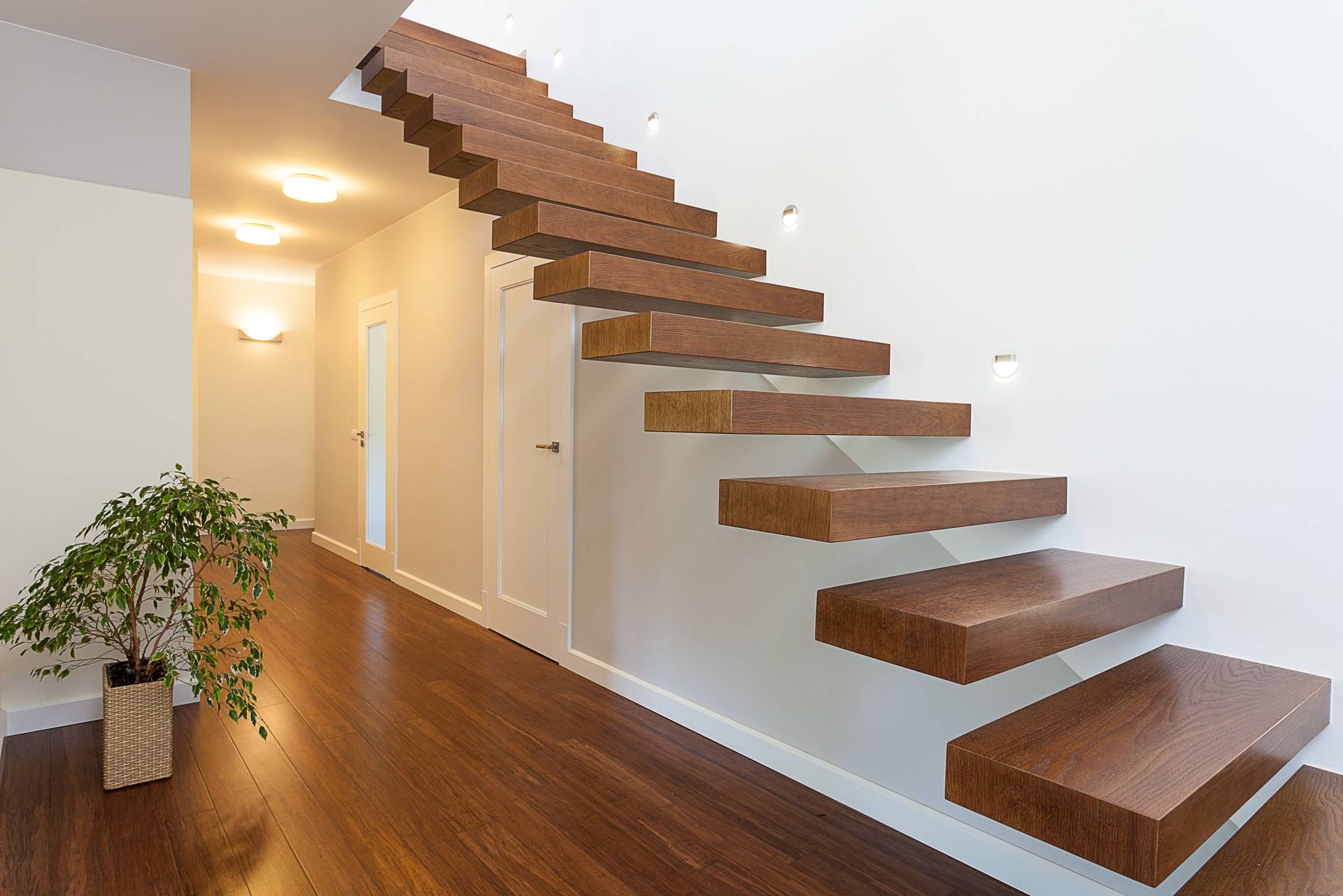 Couloir moderne avec un escalier en bois suspendu, des murs blancs et un parquet en bois foncé brillant.