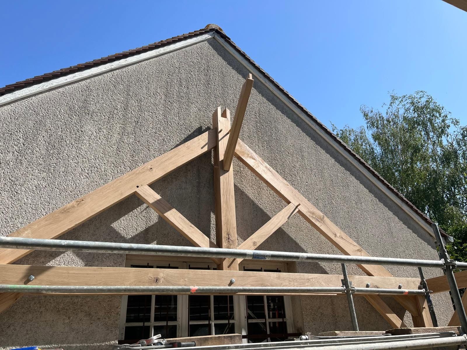 Échafaudage sur la façade d’un bâtiment en construction, avec une structure en bois sur fond de ciel bleu dégagé