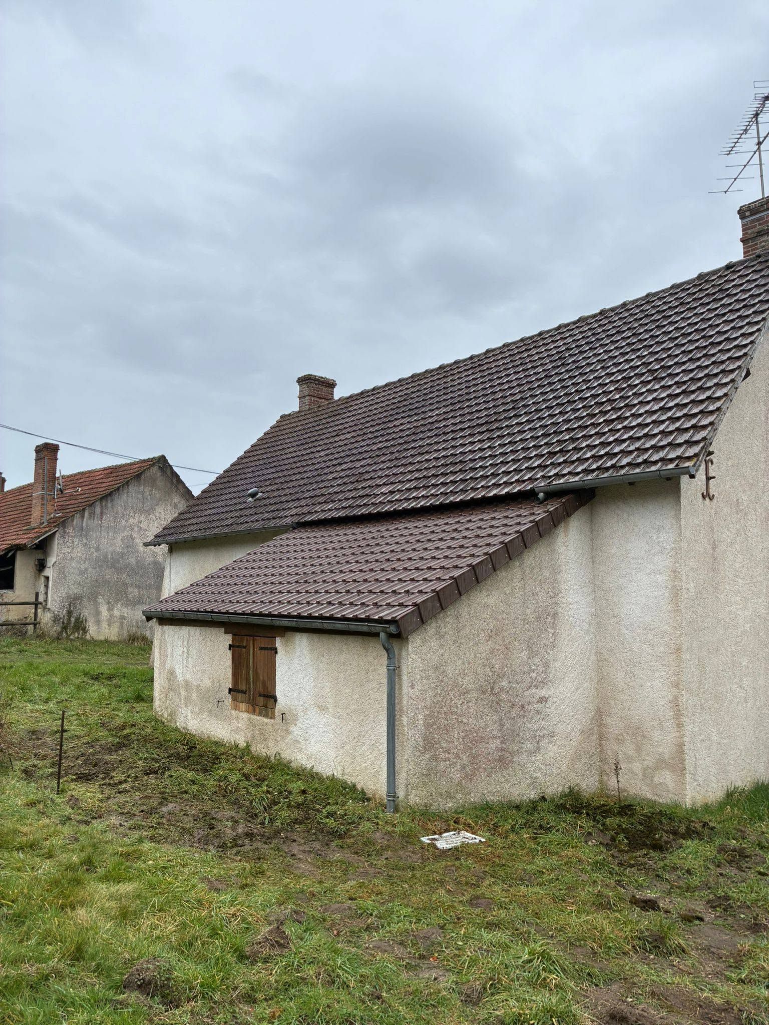 Vieille maison blanche au toit de tuiles dans un champ herbeux sous un ciel nuageux