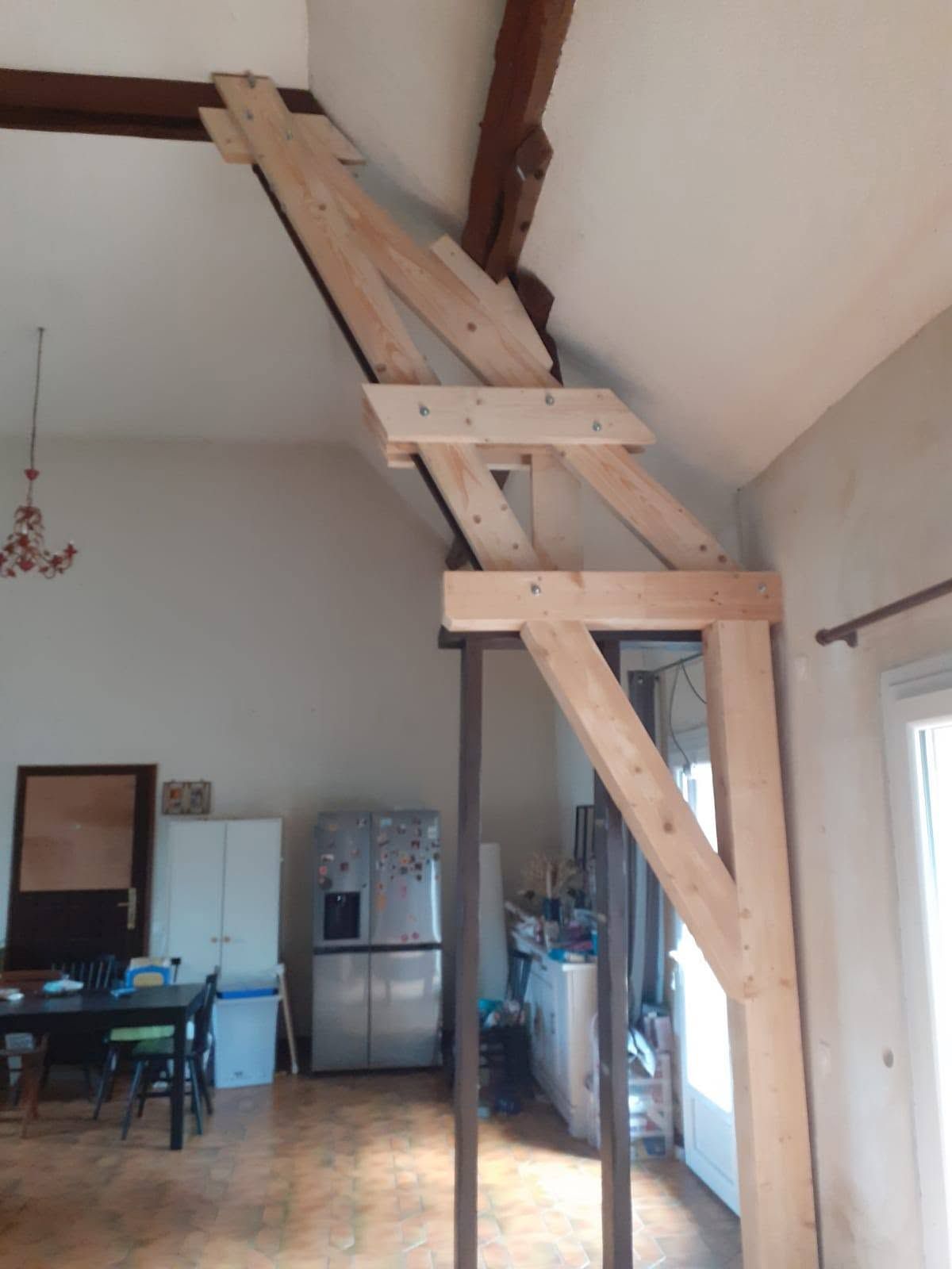 Structure d’escalier en bois adossée à un mur dans une pièce lumineuse comprenant une salle à manger et une cuisine.