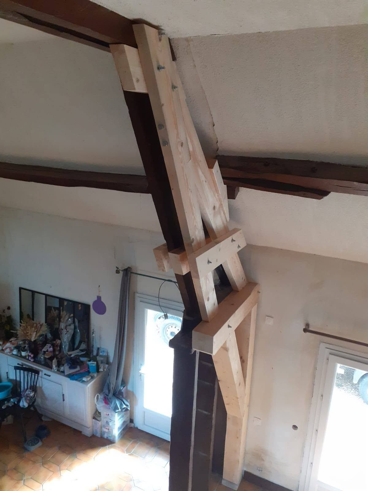 Poutre en bois effondrée suspendue au plafond d’un salon, avec des débris sous l’ouverture du toit.