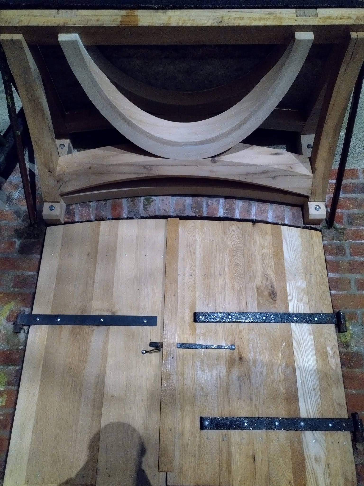 Trappe d’accès en bois d’un tonneau, avec des cerclages métalliques et des douves incurvées, dans une cave ou un atelier.