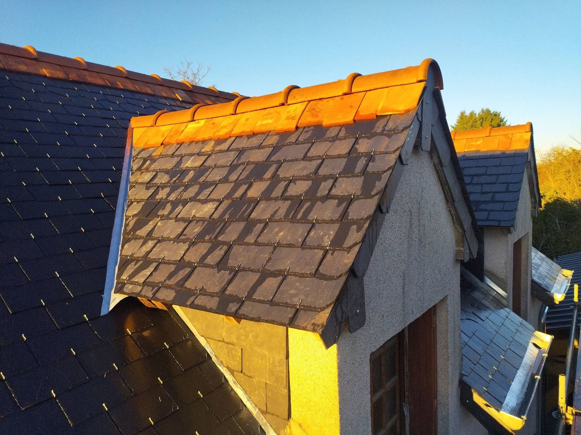Une rangée de lucarnes baignées de soleil, aux bardeaux foncés et au bardage gris, sous un ciel bleu