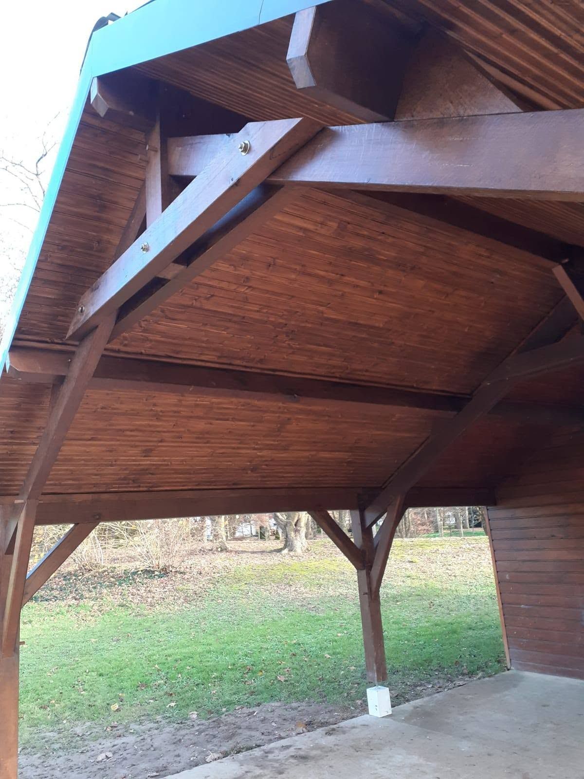 Pavillon en bois ouvert sur l’extérieur, avec un toit en pente et des poteaux de soutien, sur une pelouse verdoyante