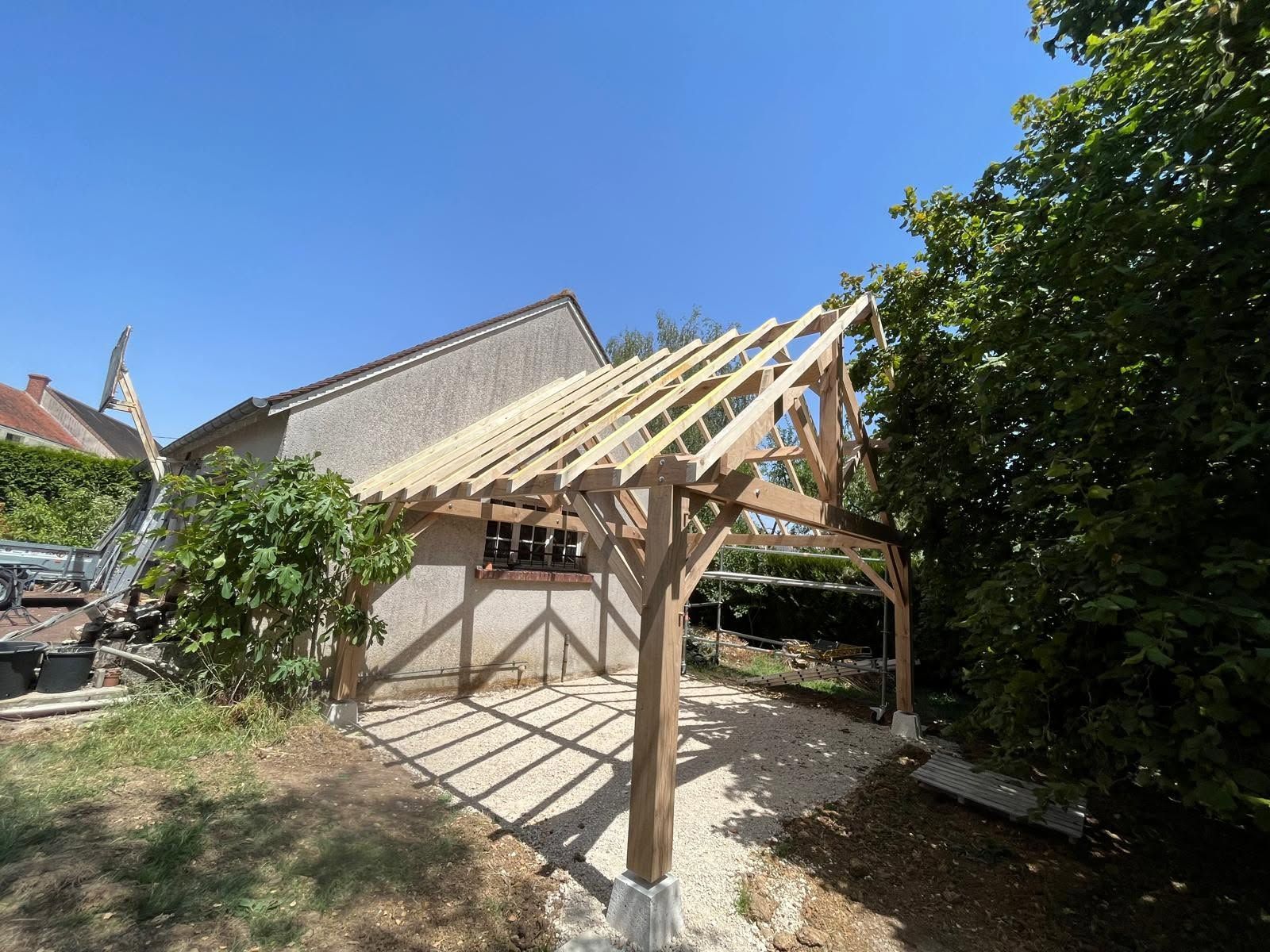 Charpente de toiture de terrasse en bois en cours de construction près d’une maison dans un jardin ensoleillé