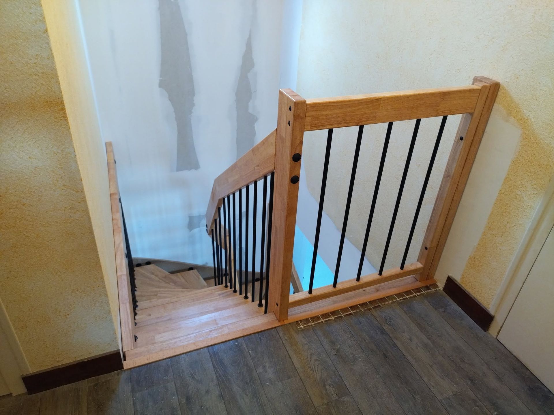 Cage d’escalier avec une barrière de sécurité en bois en haut des marches, vue depuis un couloir.