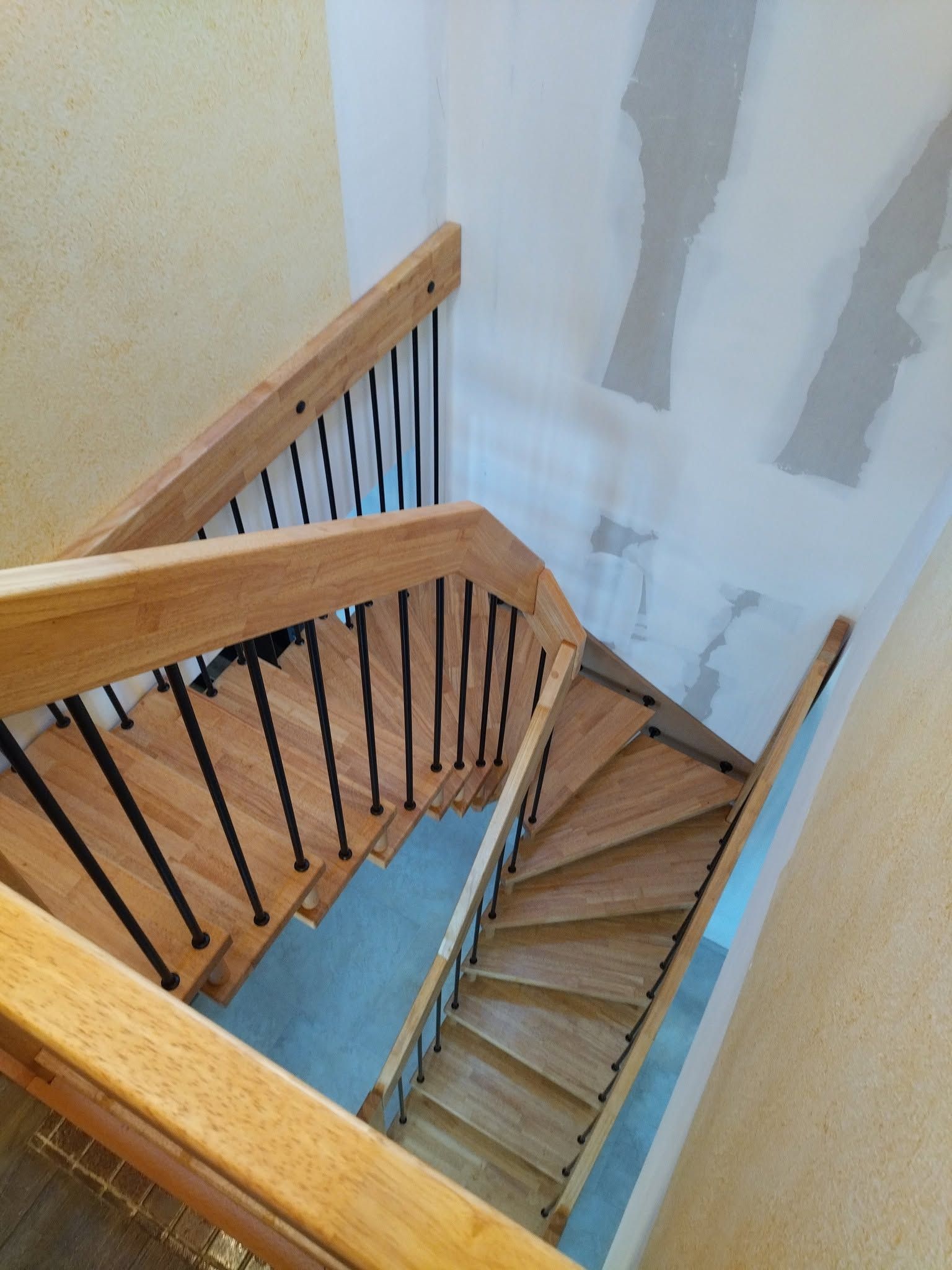 Escalier en bois avec des barreaux noirs descendant le long d’un mur blanc dans un angle intérieur étroit