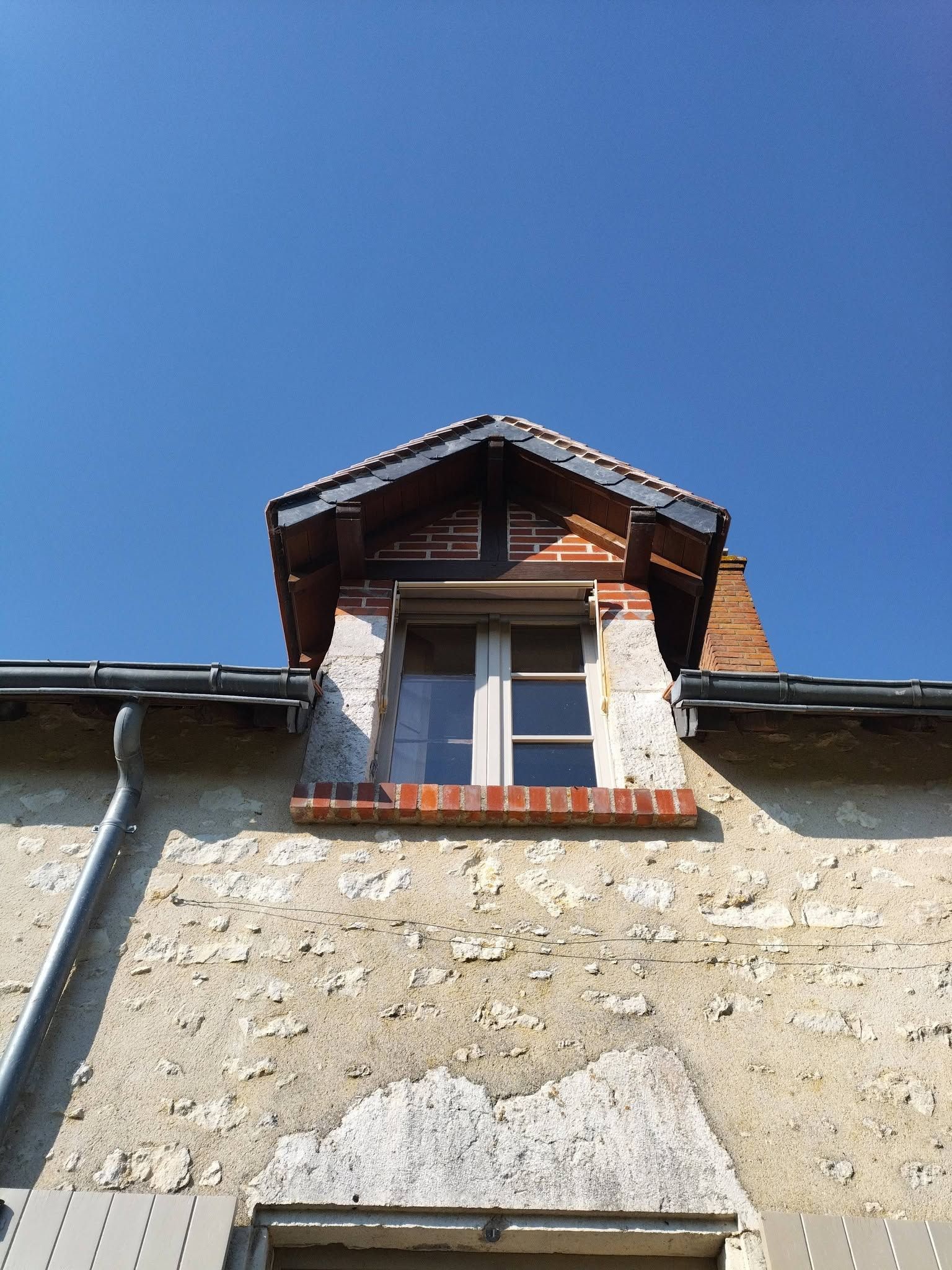 Mur en pierre d’une maison avec une petite lucarne sous un ciel bleu