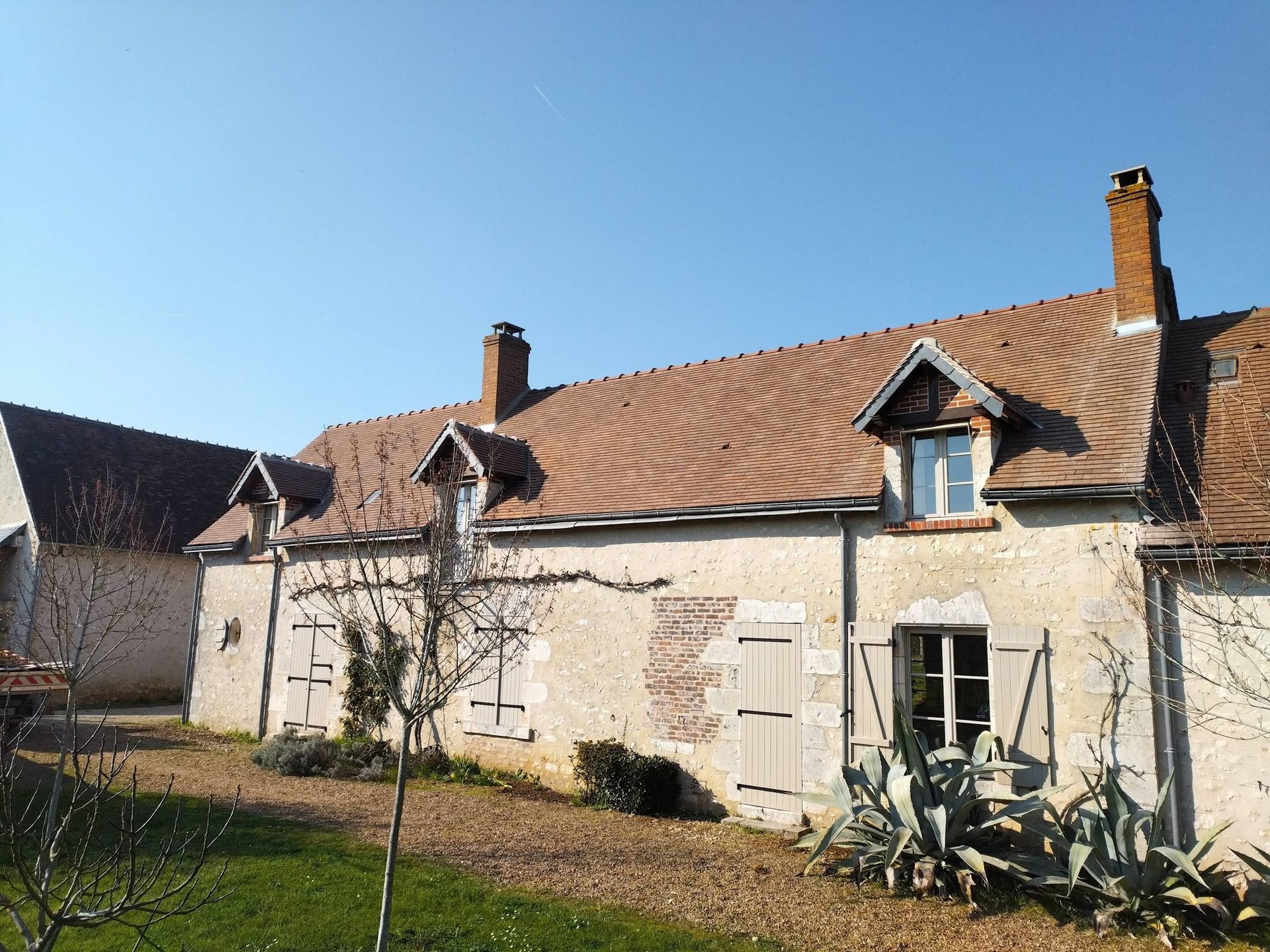 Maison rustique couleur crème, avec un toit en tuiles rouges et des fenêtres mansardées, sous un ciel bleu