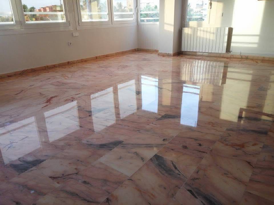 Suelo de mármol rosa pulido que refleja la luz del sol que entra por las ventanas.