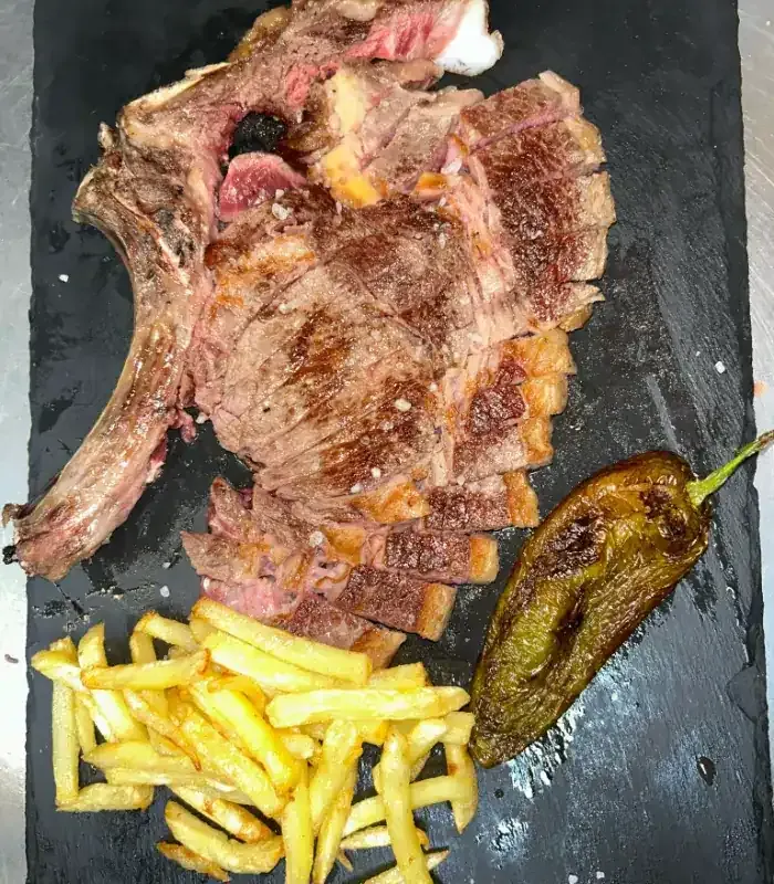 Carne a la parrilla cortada en dados sobre un plato de pizarra negra con una rodaja de limón y una taza de salsa de naranja.