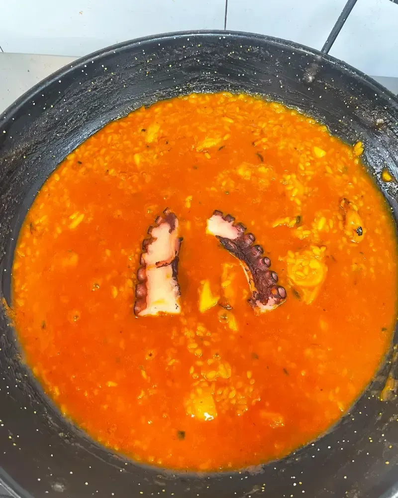 Paella de marisco en un bol blanco con gambas, mejillones y pimientos rojos sobre una mesa de madera.