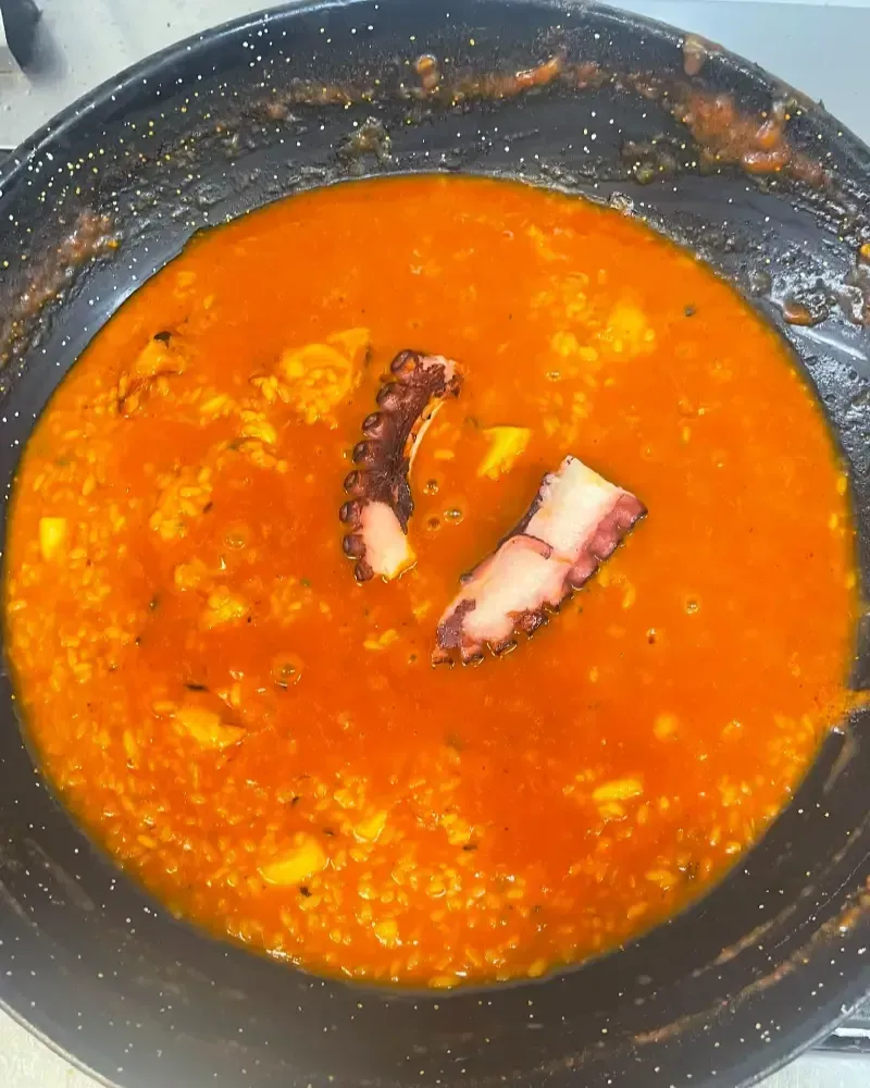 Paella de marisco colorida en una paellera grande, con gambas, mejillones y rodajas de limón.