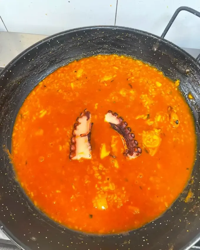 Paella de marisco colorida en una paellera grande, con gambas, mejillones y rodajas de limón.