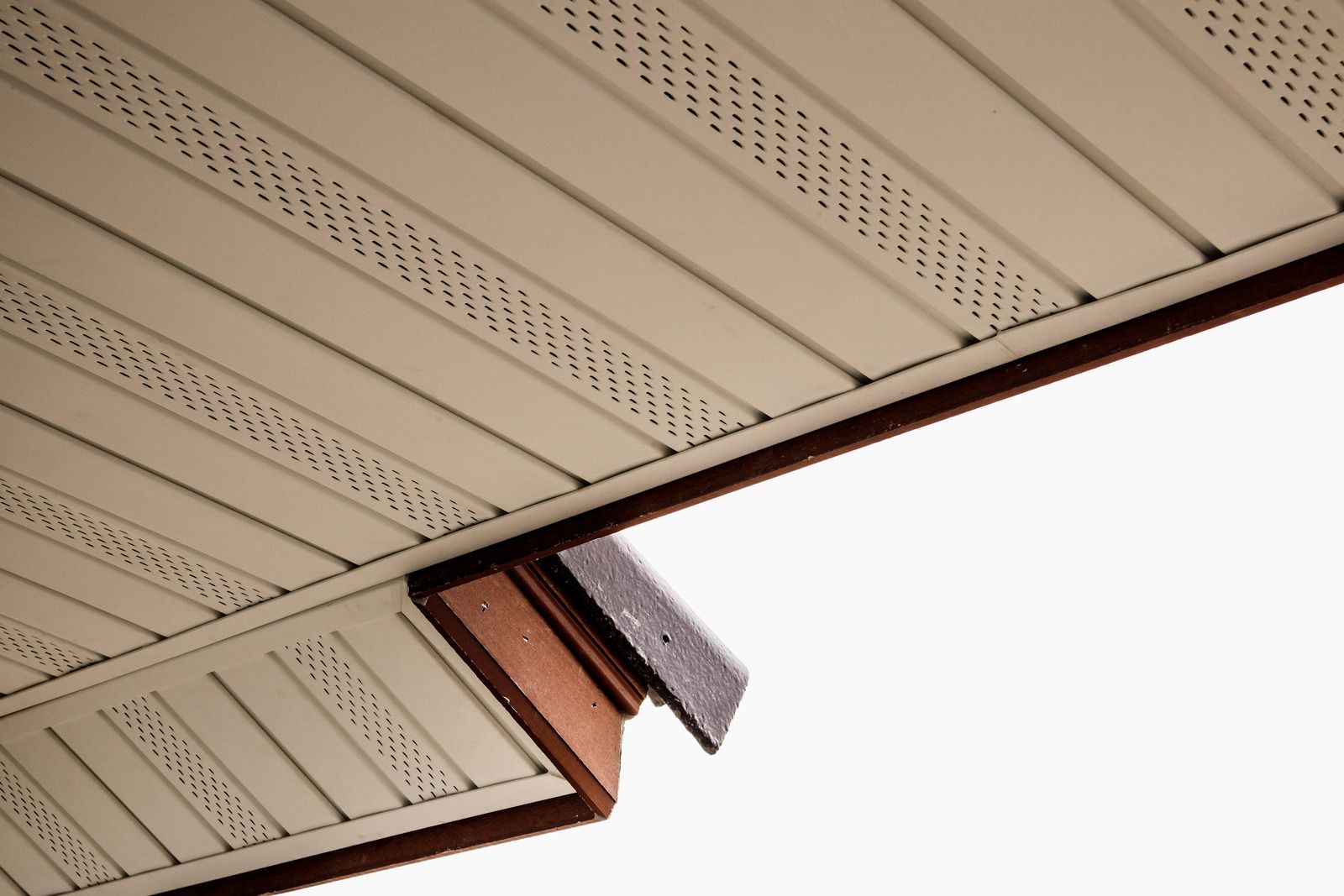 Close-up of beige house soffit and brown fascia at a roof corner against a white sky