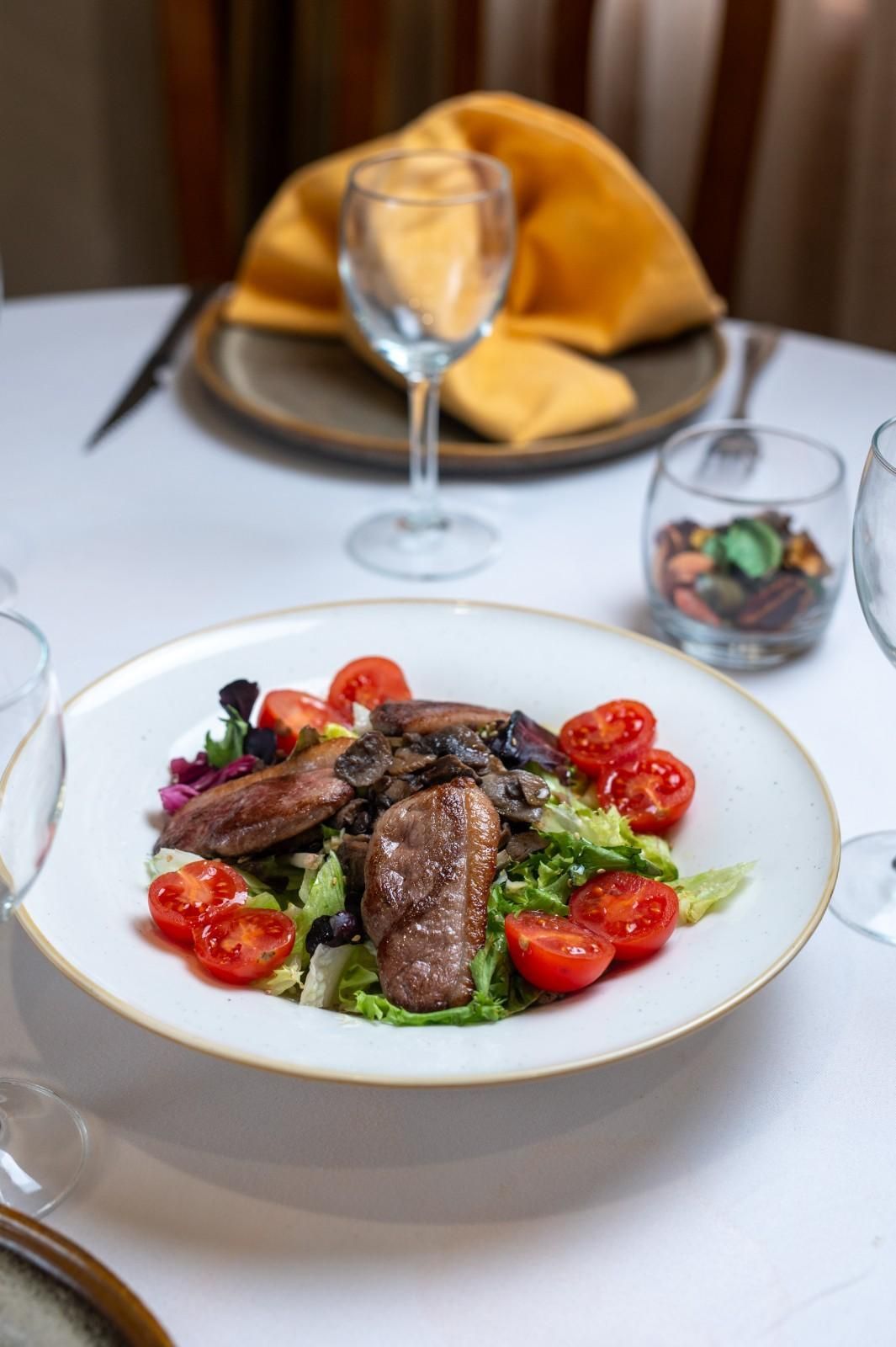 Mesa de restaurante con un filete emplatado y fresas, una copa de vino y una servilleta doblada al fondo.