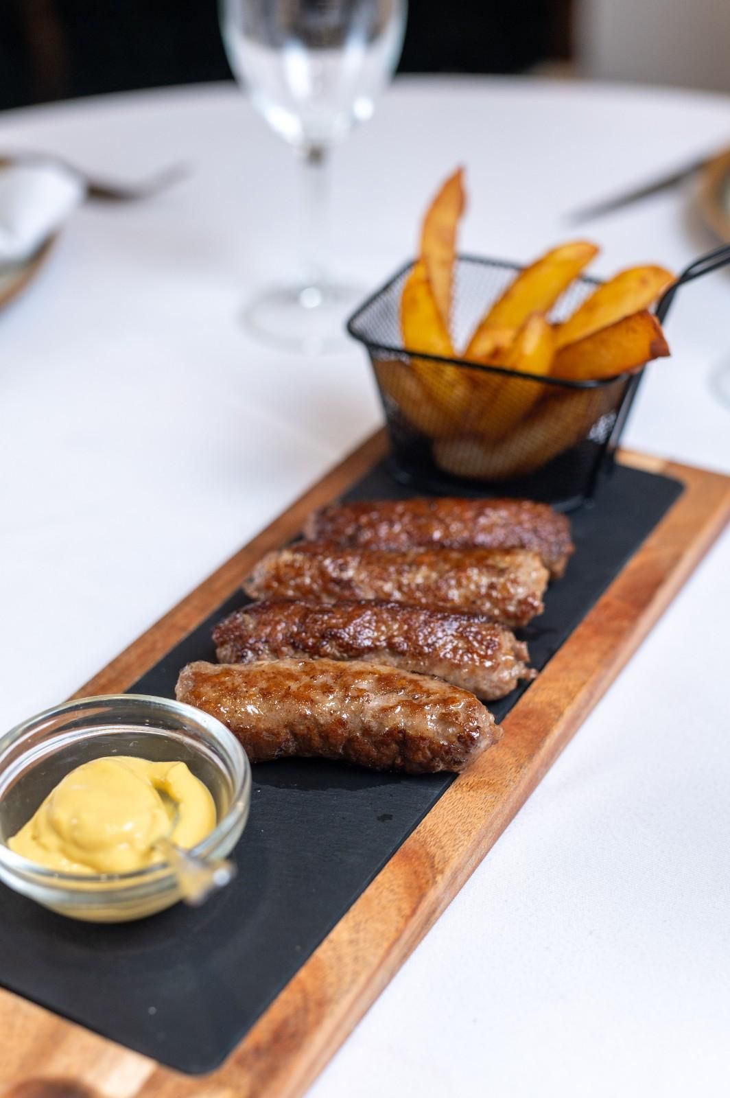 Salchichas a la parrilla con patatas fritas y mostaza servidas en una tabla de madera larga en un restaurante.