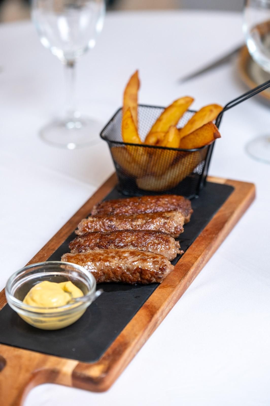 Filete en rodajas con patatas fritas en una tabla de madera con mostaza sobre un mantel blanco.