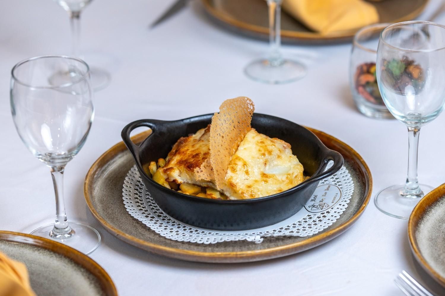 Postre horneado con helado en una fuente de hierro fundido sobre una mesa blanca, flanqueada por copas de vino.