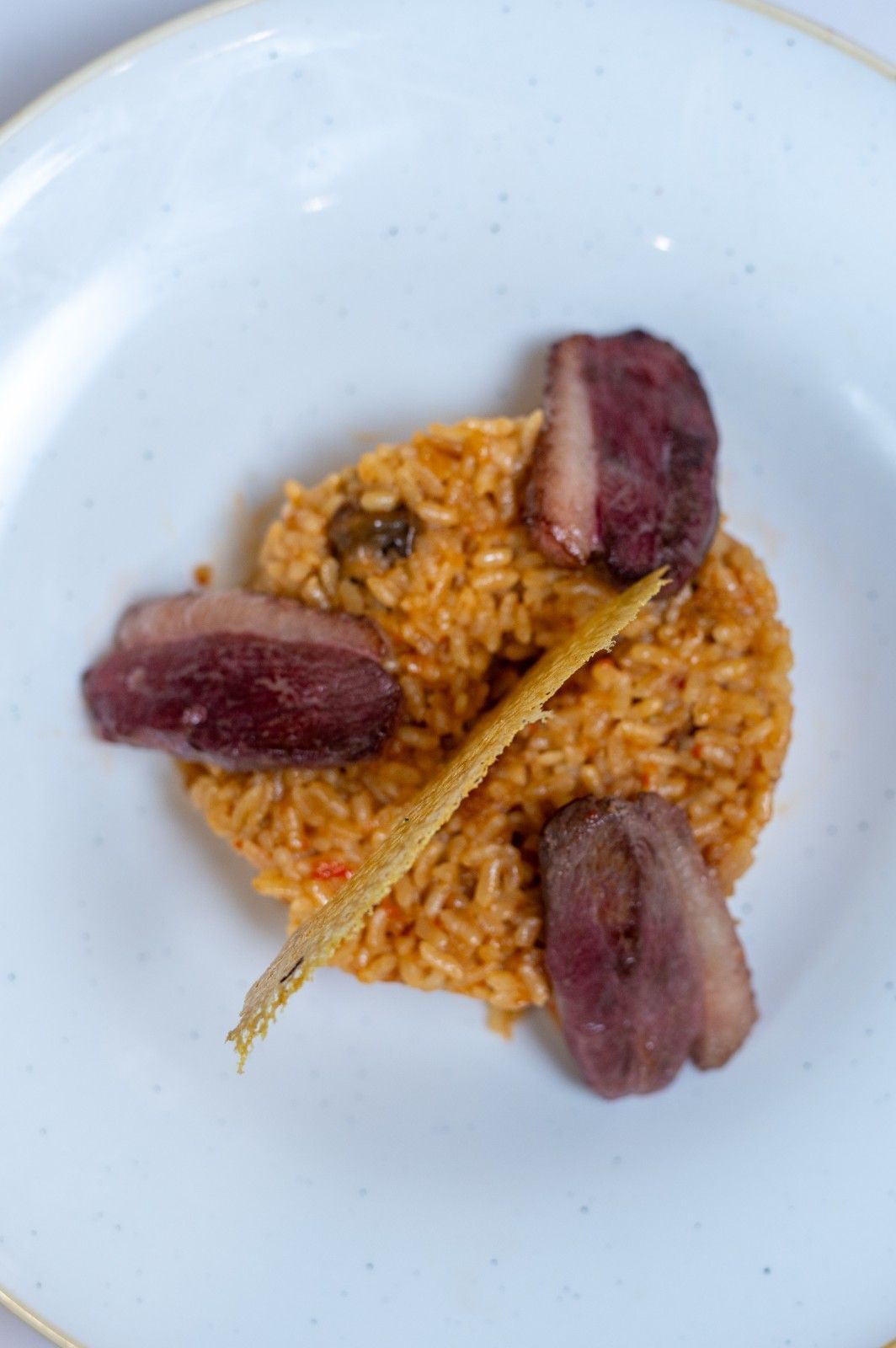 Plato blanco con una pequeña porción de arroz cubierta con tres trozos de carne sellada y una guarnición fina parecida a una pajita.