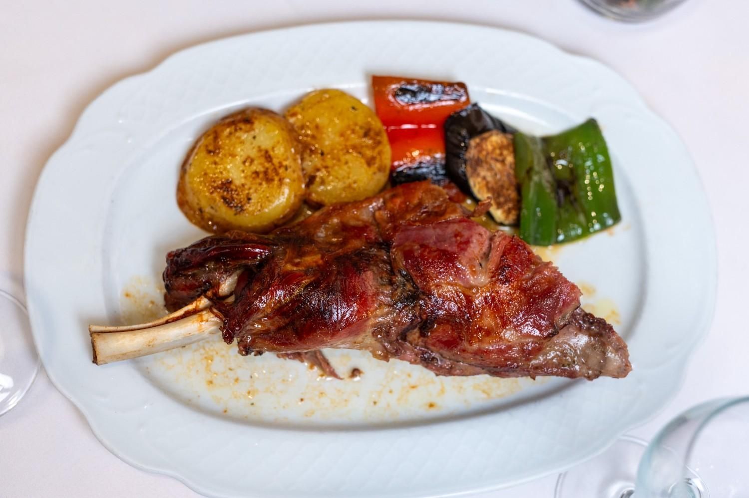 Carne asada emplatada con patatas, pimiento rojo y judías verdes en un plato blanco.