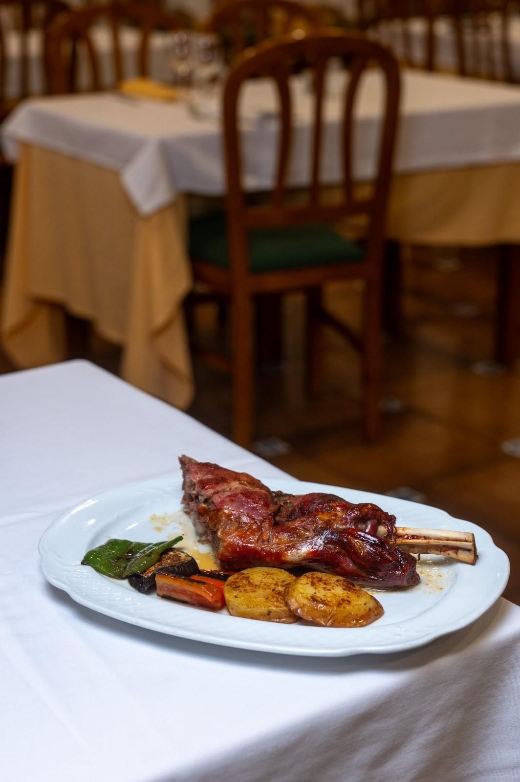 Carne a la parrilla con patatas asadas y verduras sobre un mantel blanco en un restaurante.