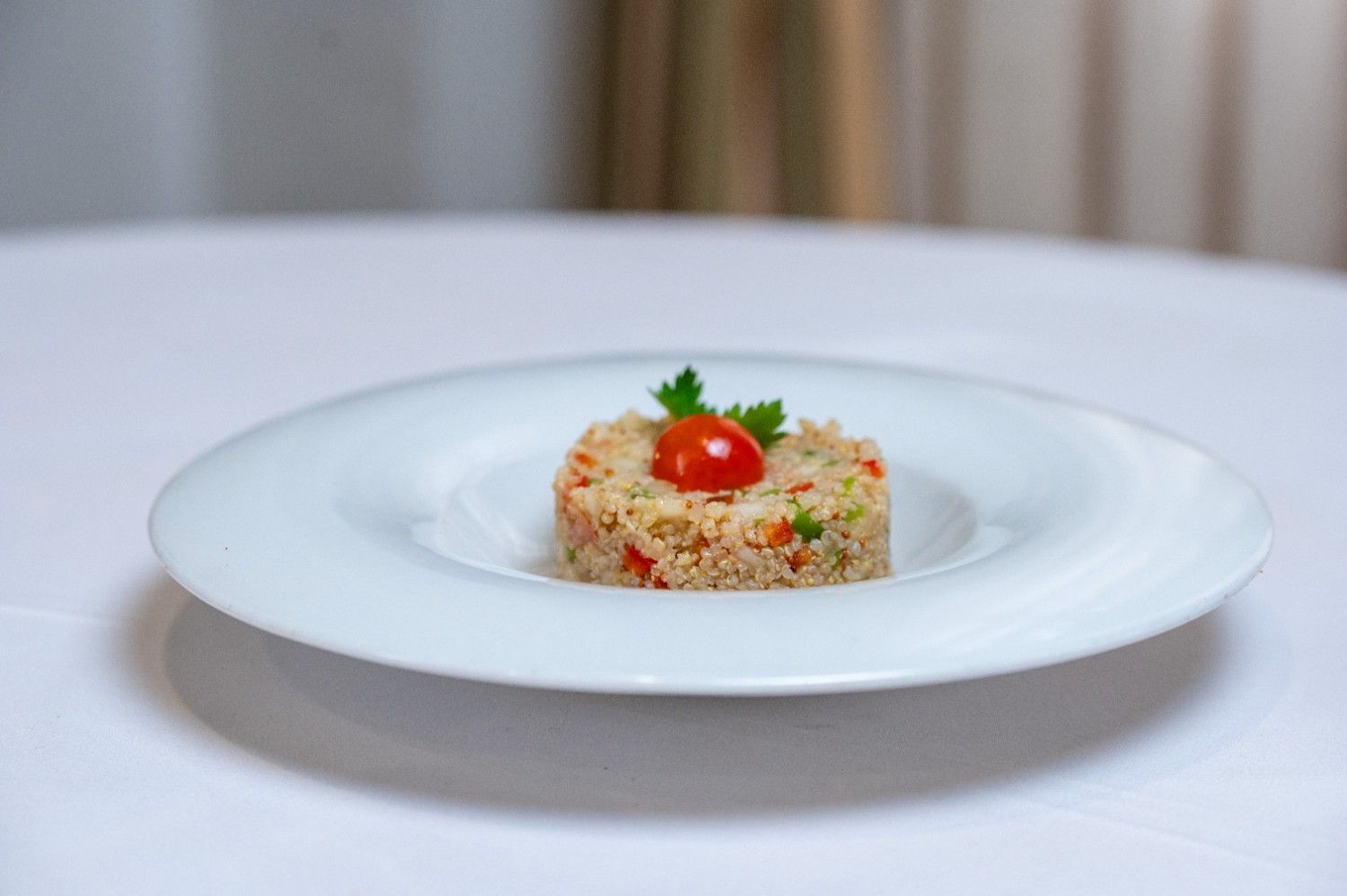 Plato de arroz gourmet emplatado, adornado con un tomate cherry y hierbas aromáticas sobre un mantel blanco.