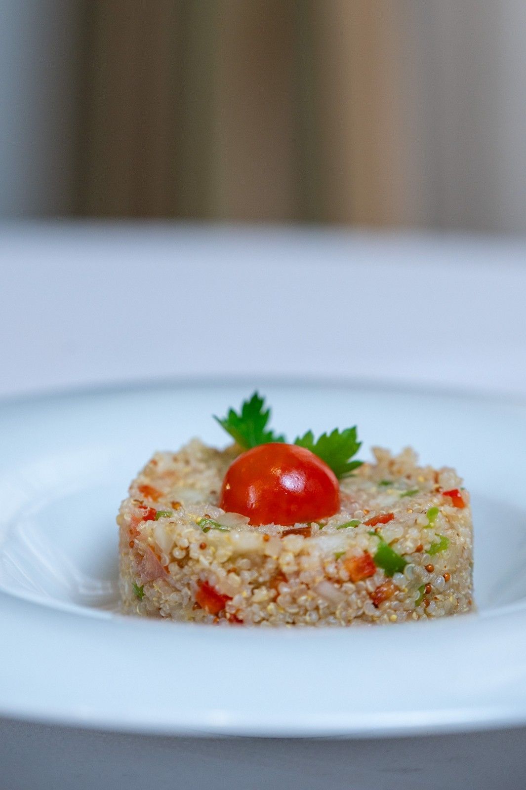 Ensalada de quinoa moldeada en un plato blanco, coronada con un tomate cherry y una hoja de perejil.