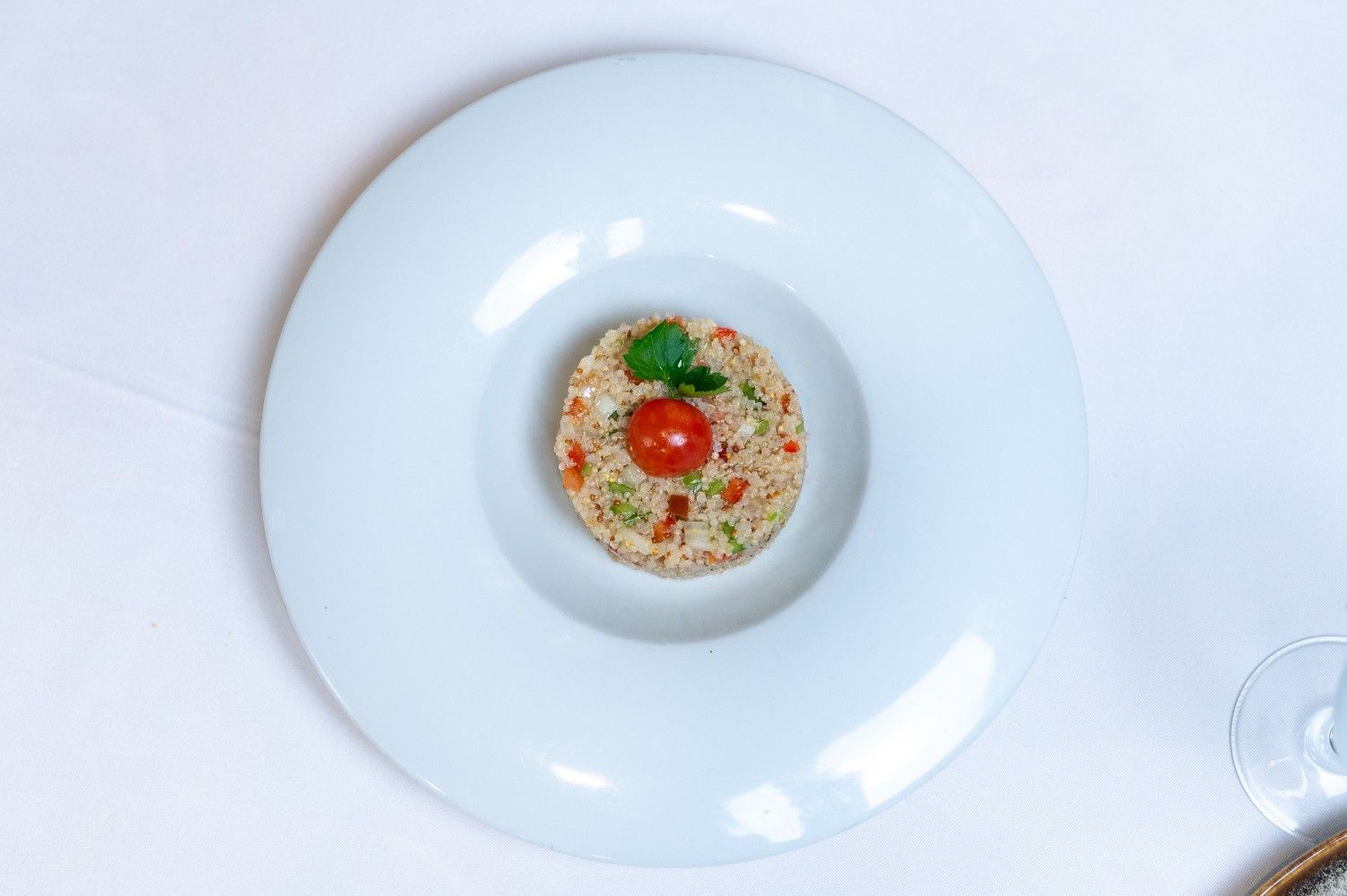 Vista aérea de un plato gourmet emplatado en un cuenco blanco, adornado con hierbas y una rodaja de tomate rojo.