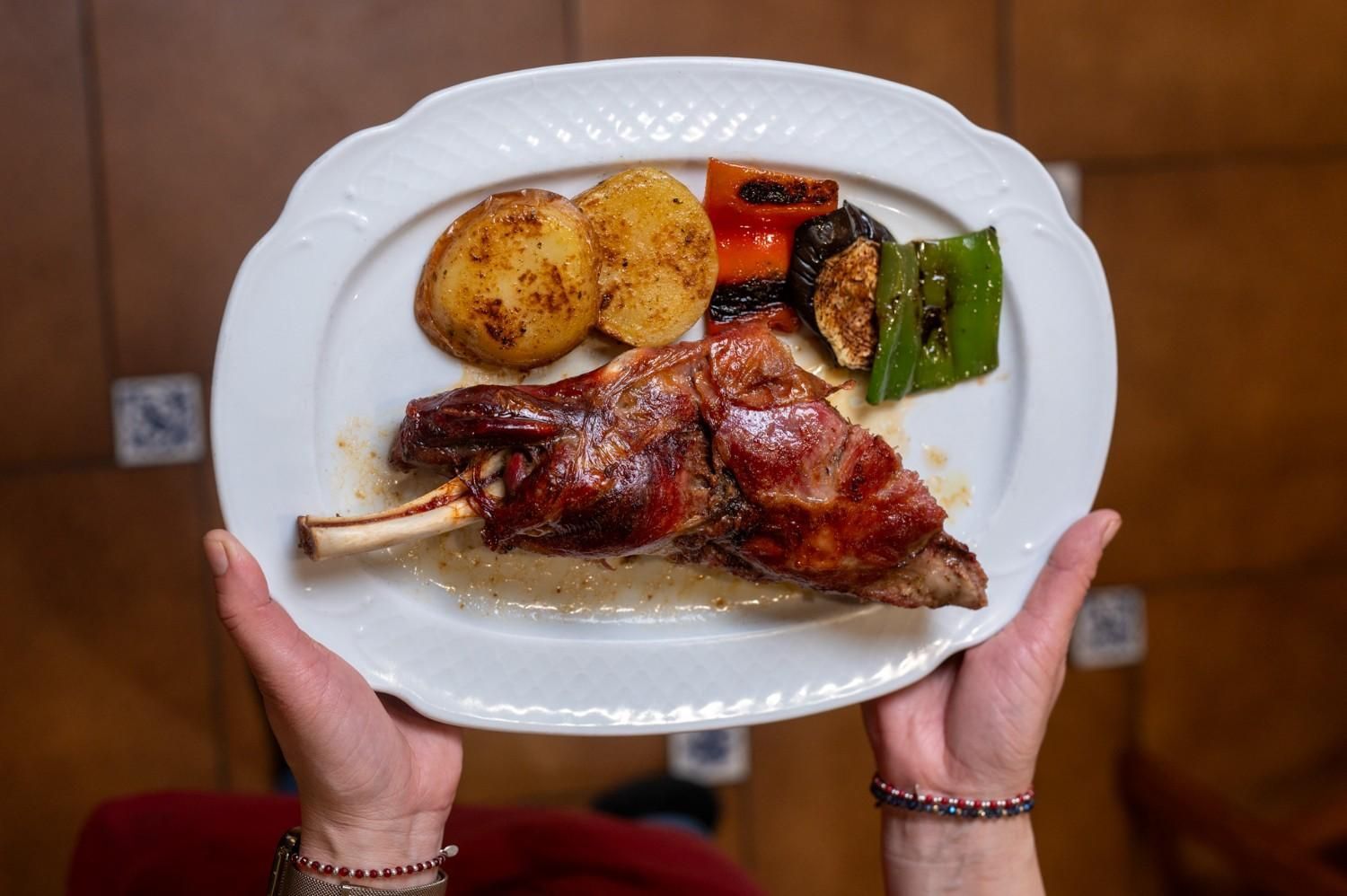 Carne asada con patatas y verduras en un plato blanco sostenido con ambas manos.