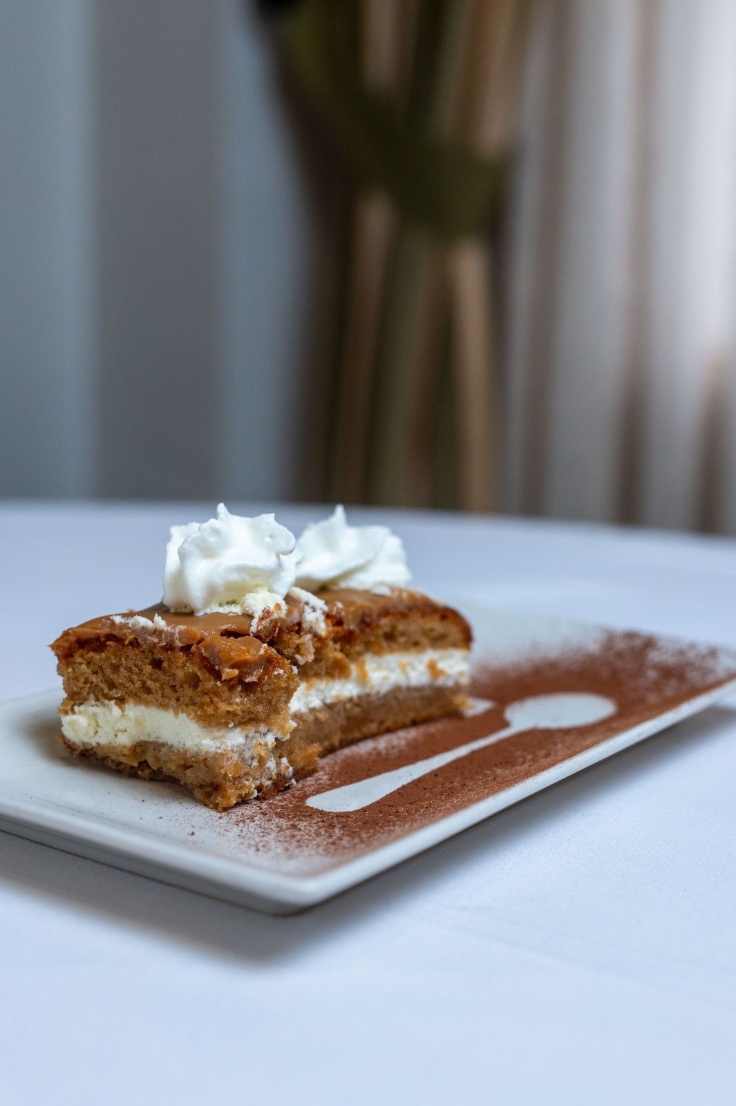Porción de postre en capas con crema batida en un plato blanco, espolvoreado con cacao en polvo.