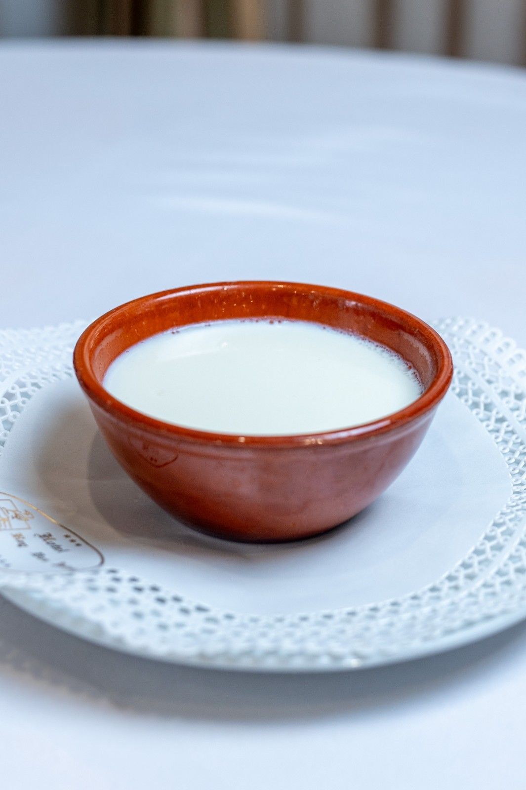 Bol de cerámica marrón para la leche sobre un plato de encaje blanco.