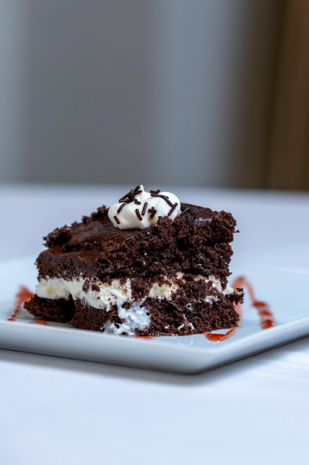 Porción de pastel de chocolate con crema batida en un plato blanco, decorada con virutas de chocolate.