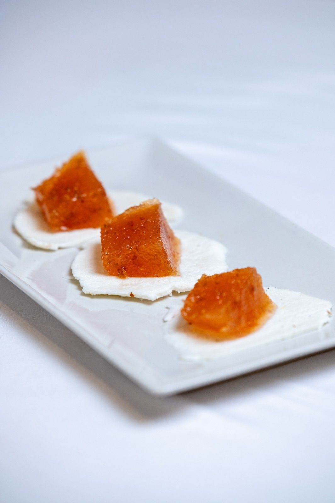 Tres cuadrados de gelatina de naranja sobre un plato rectangular blanco con adornos blancos.