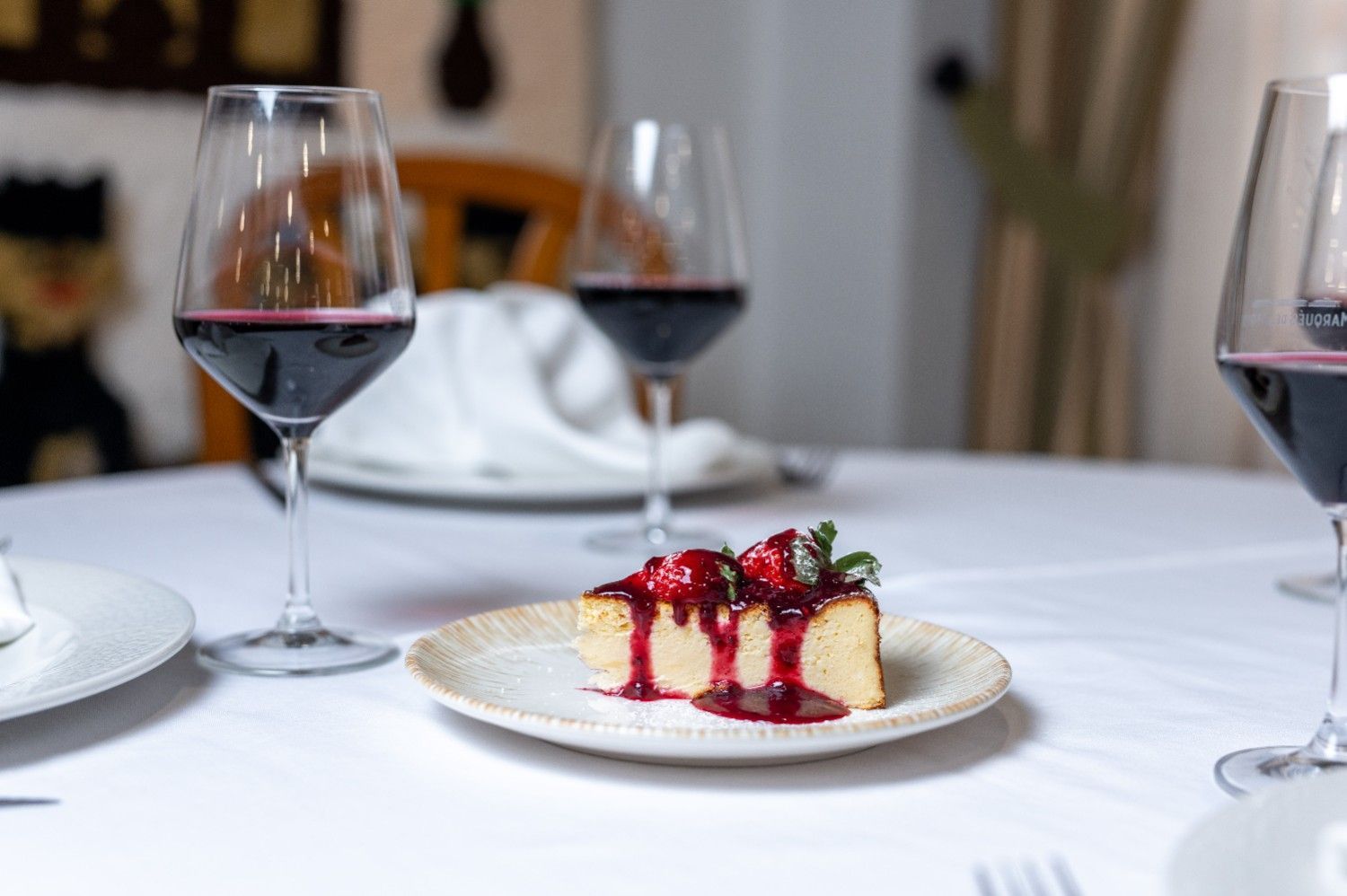 Un postre sobre un mantel blanco con copas de vino tinto en un restaurante con iluminación tenue.