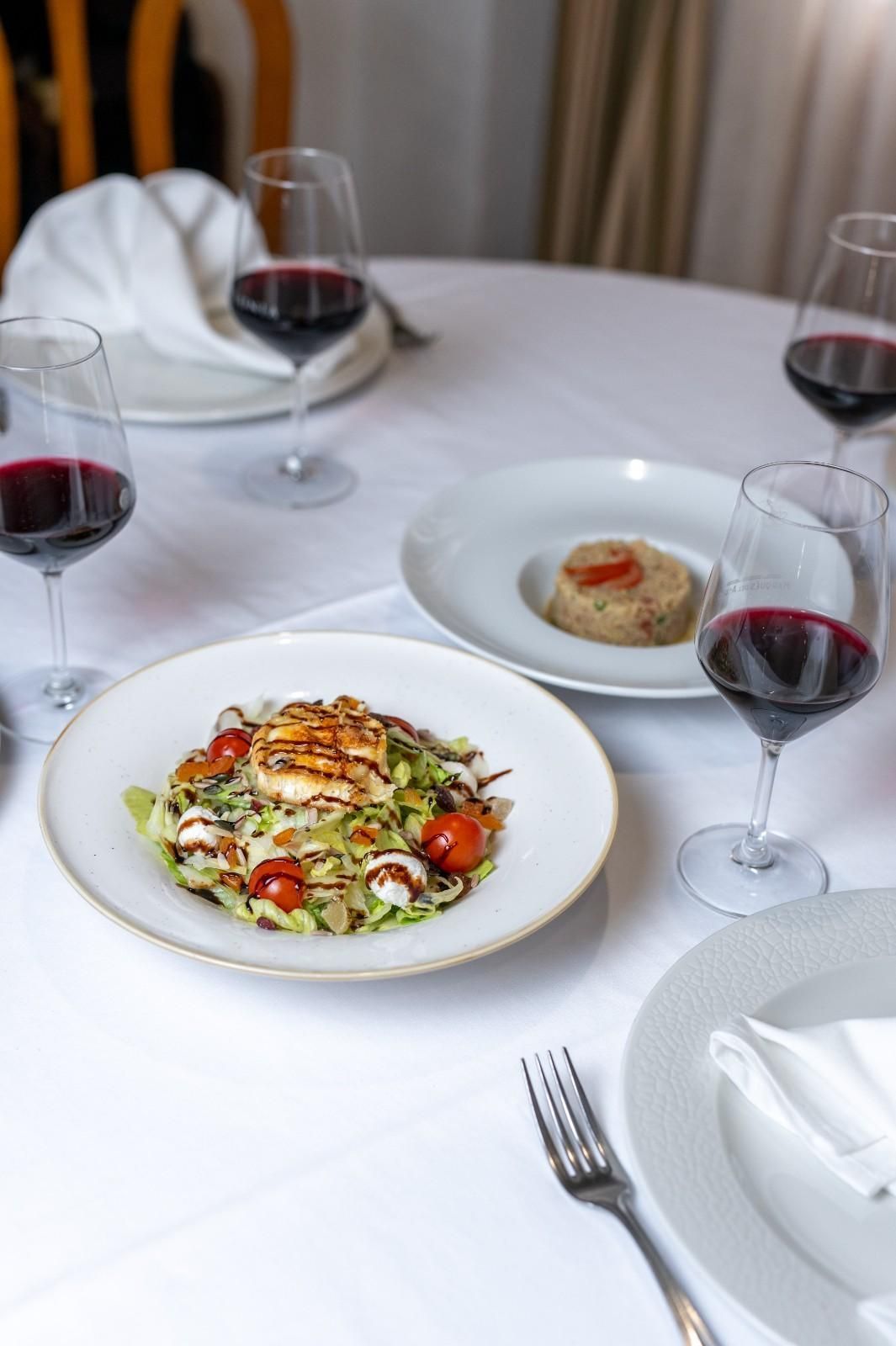 Elegante mesa de comedor con pasta, hummus, copas de vino tinto y servilletas blancas.